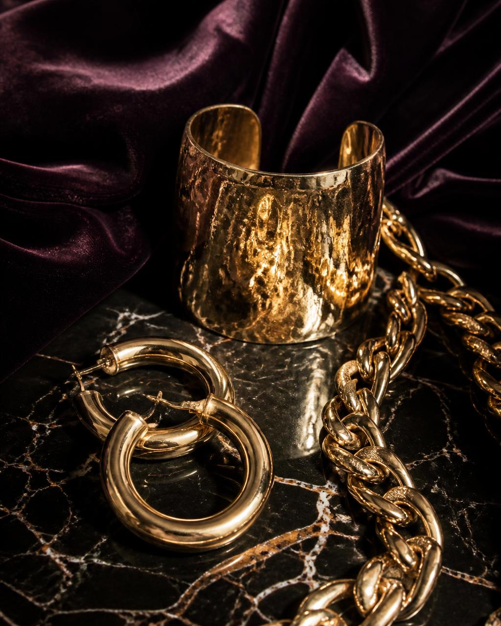 Statement gouden sieraden op donker marmer met aubergine fluweel
